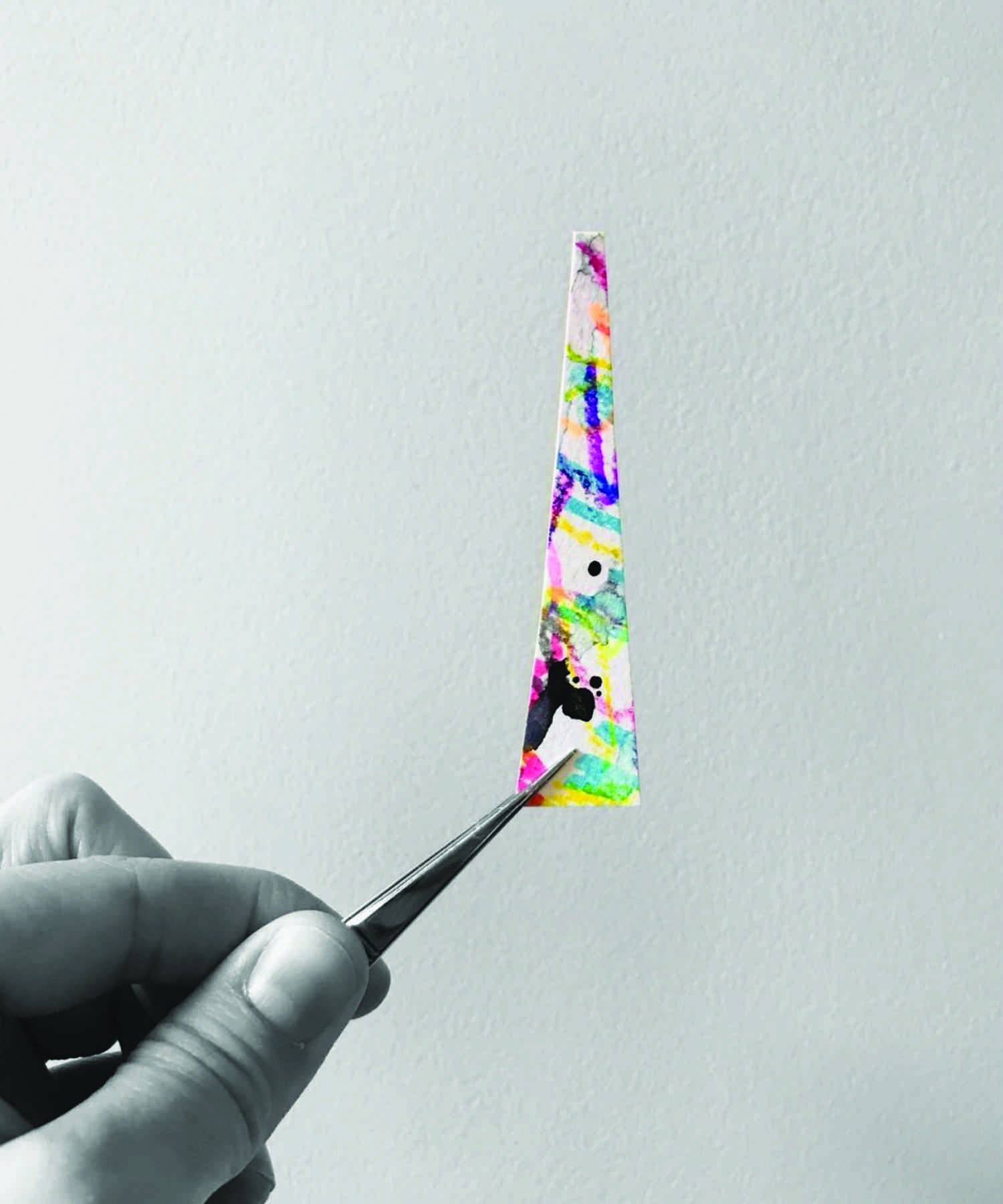 Hand holding coloured piece of paper with tweezers